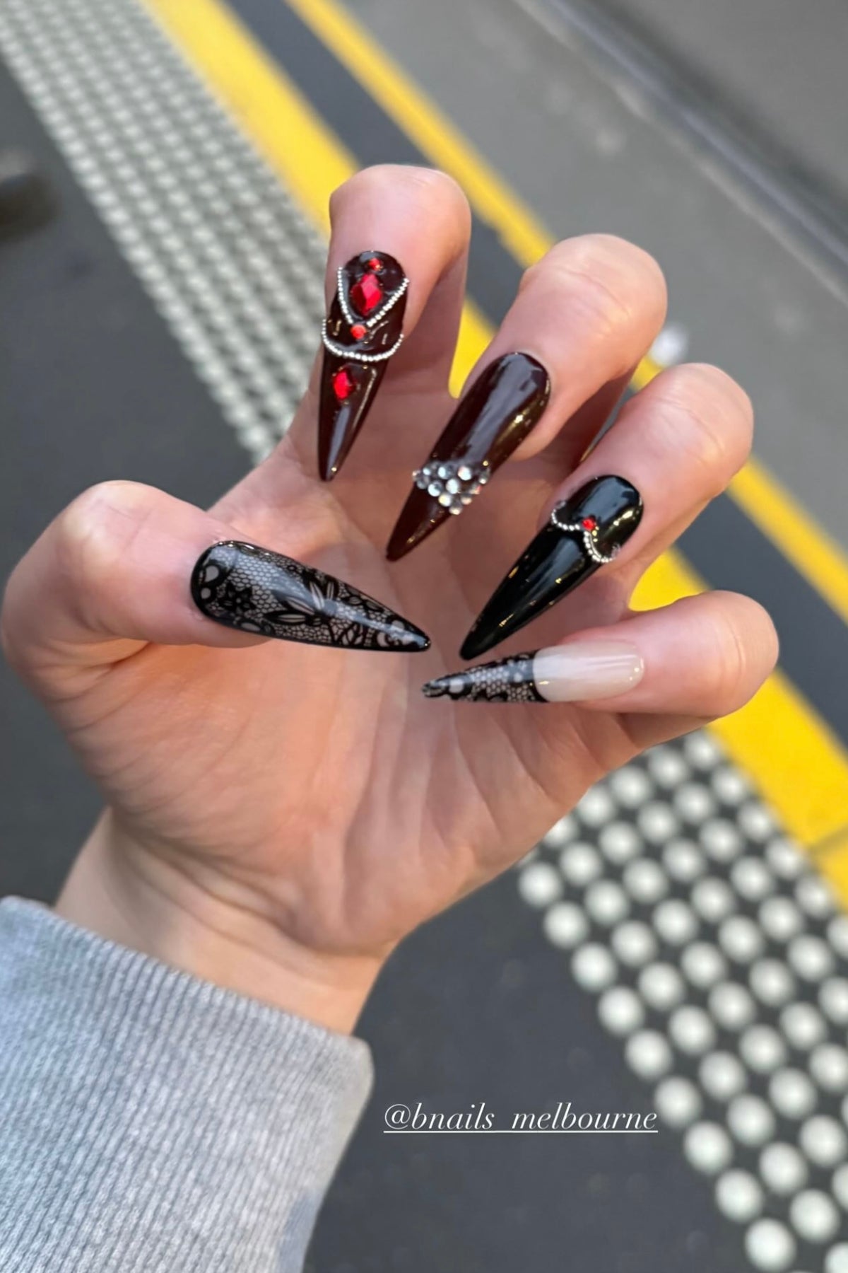 Customer wearing black and red pointed press-on nails with gem details