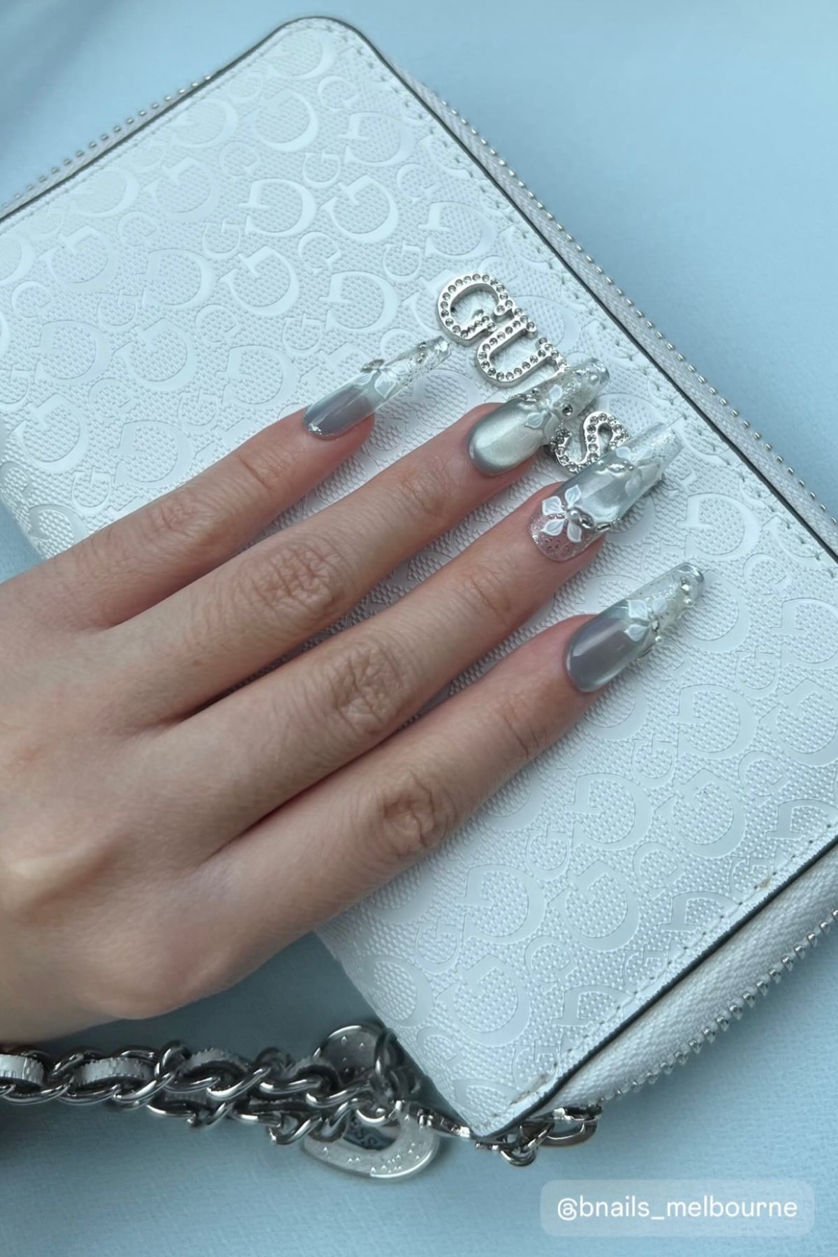 Customer wearing silver-toned long press-on nails with a white bag