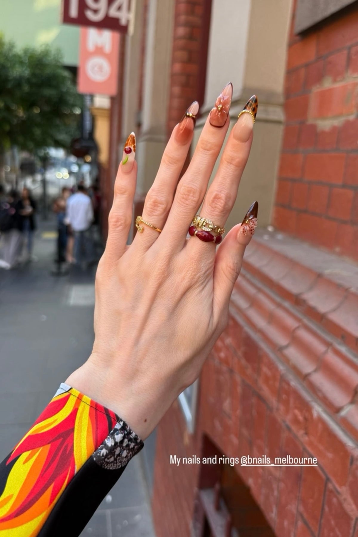 Customer wearing warm-toned pointed press-on nails with rings on a city street