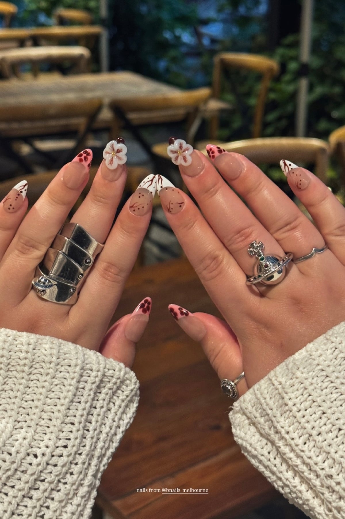 Customer showing floral press-on nails on both hands at a cafe