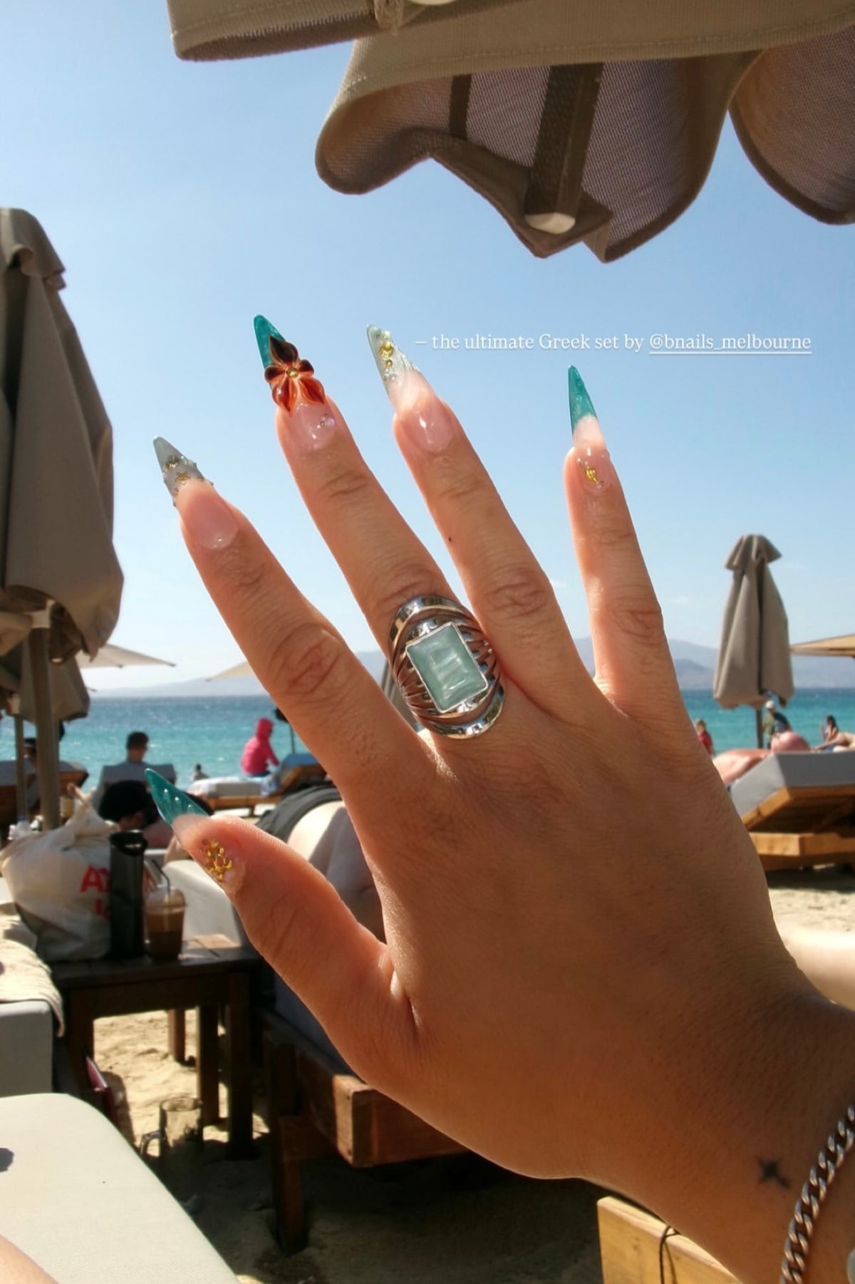 Customer wearing green and gold decorated press-on nails by the sea