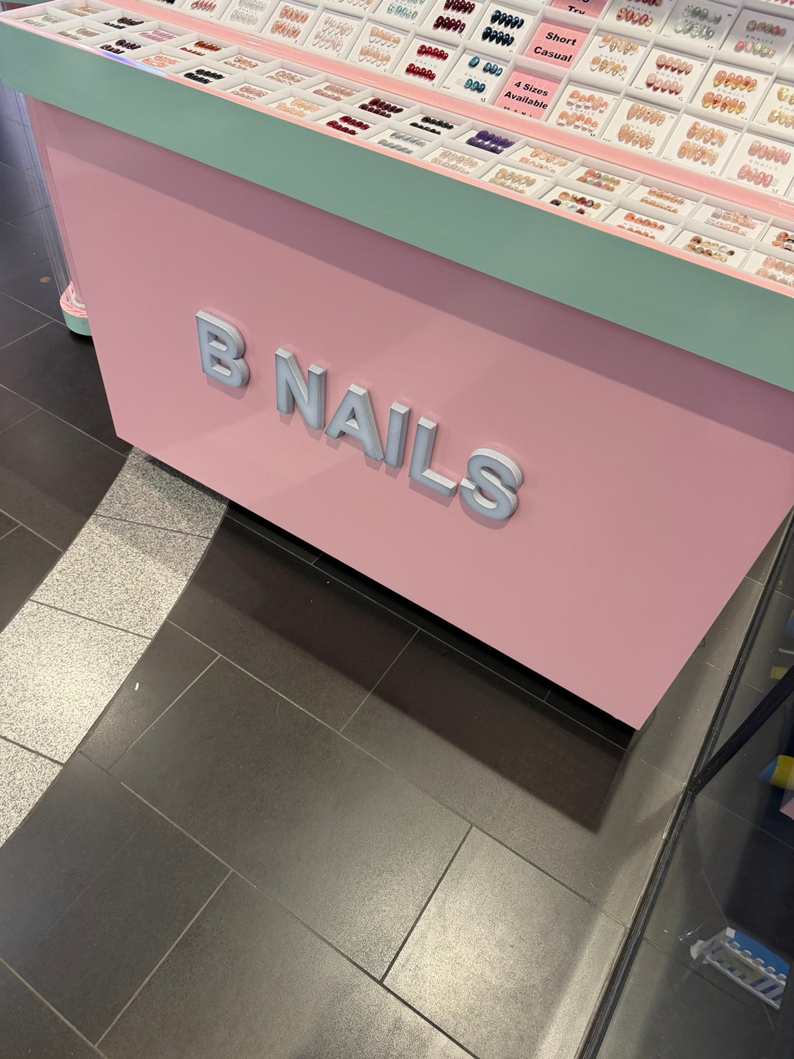 Press-on nail designs displayed on a pink and mint BNAILS counter